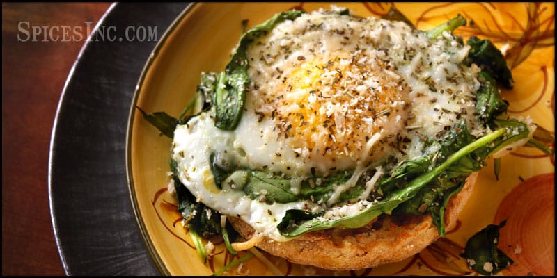 english muffin, baked egg with spincah resting on top of it, black pepper and sprigs of green rosemary seasonings visible too