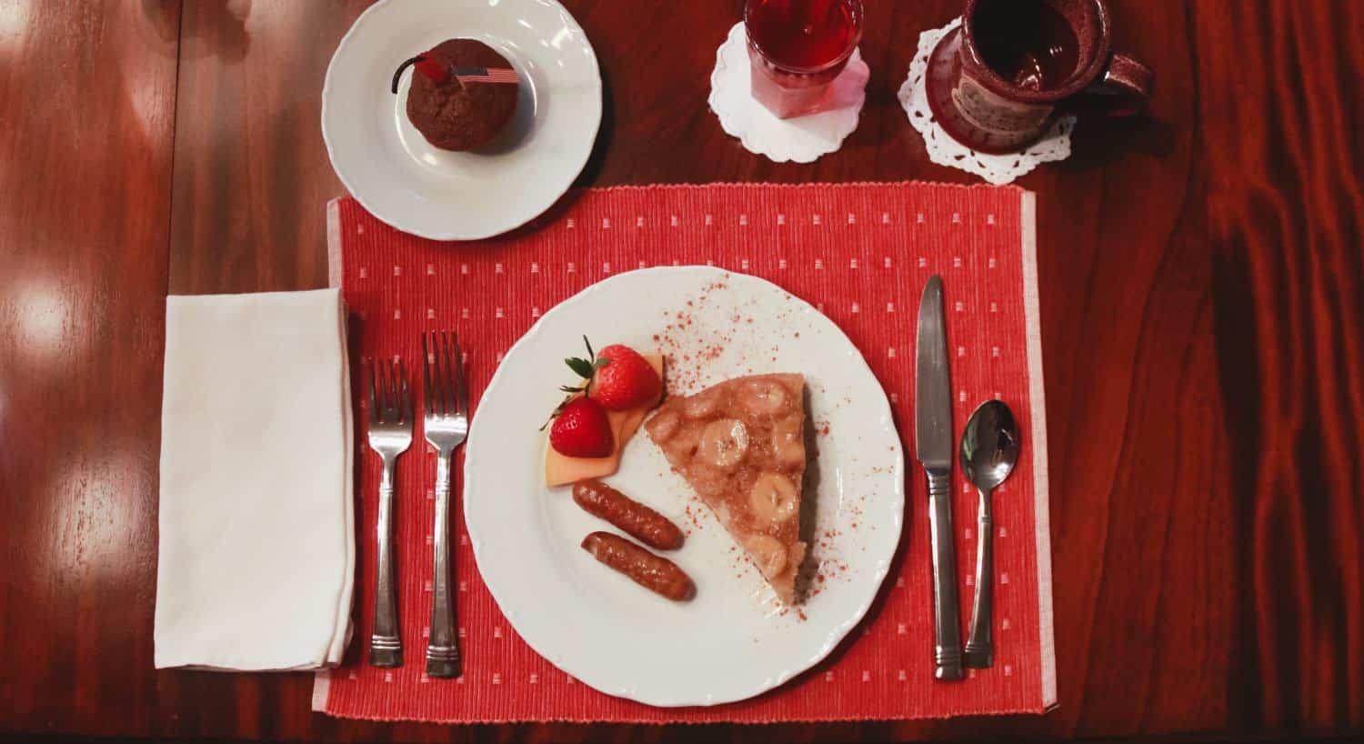 Red placemat and white napkin on wooden table with breakfast food on a white porcelain plate