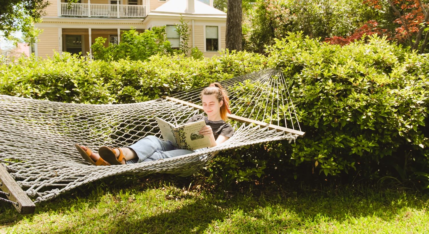 Girl reading a book and relaxing in a large hammock surrounded by green bushes