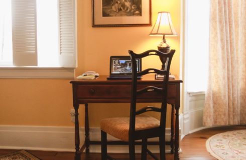 Small dark wooden desk and chair with laptop and desk lamp on top