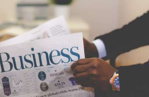 Man in black suit holding the business section of a newspaper
