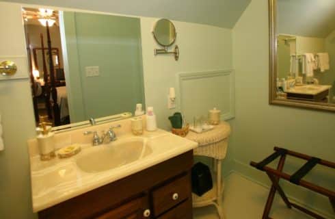 Bathroom with light green walls, dark wooden vanity with cream sink, large mirror, and wicker side table