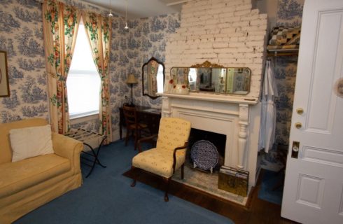 Sitting area in bedroom with white brick fireplace, yellow couch and chair, and dark wooden desk